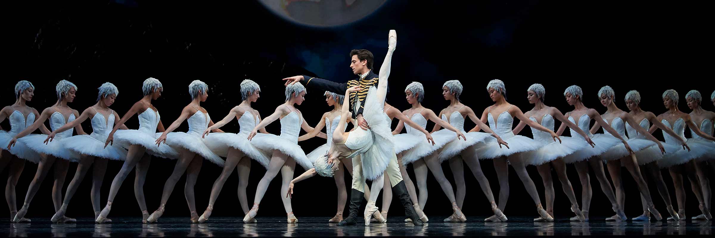 Before line of swans facing center, Siegfried faces right, holding Odette’s waist as she bends over on right leg, left leg up