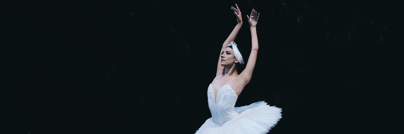 A female dancer with her arms above her head in Swan Lake