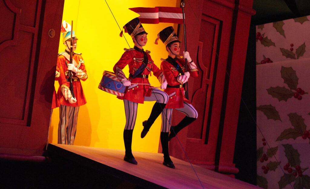 Two toy soldier officers marching out of a cabinet, one with a drum, and one holding a flag.