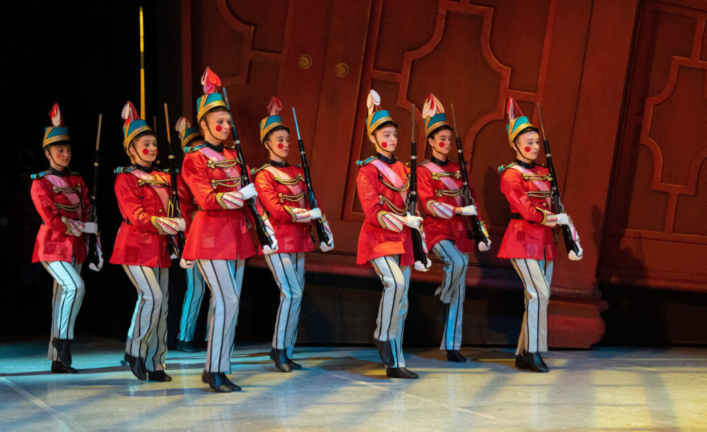 Seven infantry toy soldiers march in formation with wooden rifles shouldered.