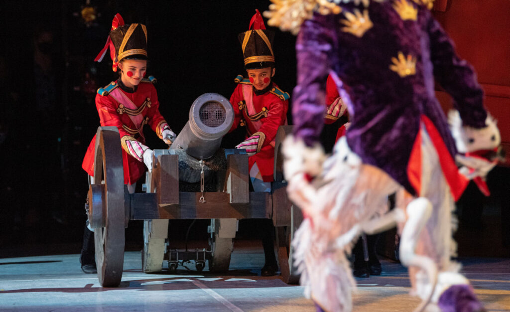 Toy soldiers wheeling in a canon towards the Mouse King, out of focus in the foreground.