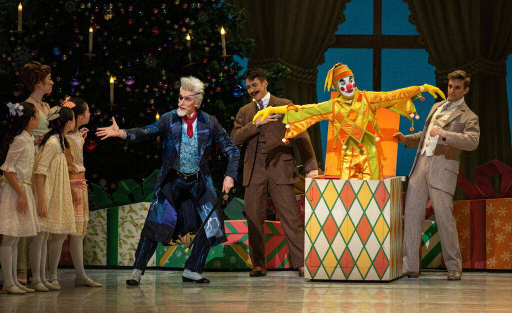 Children and adult party guests look on in amazement as Drosselmeyer presents the dancing Jack-in-the-Box doll.